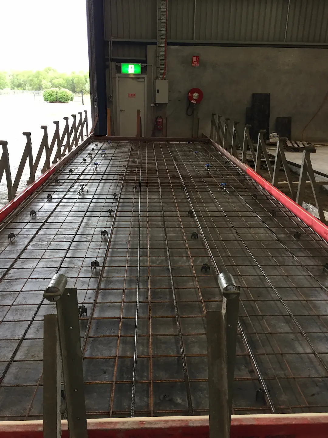 Close-up of the reinforcing bar framework within a formwork setup for a tilt panel at the Brisbane storage facility. The dense grid of rebar is meticulously arranged to reinforce the concrete, ensuring structural integrity. Visible in the background is the partially open industrial door that leads to the outdoors, highlighting the juxtaposition of construction and the natural environment outside.