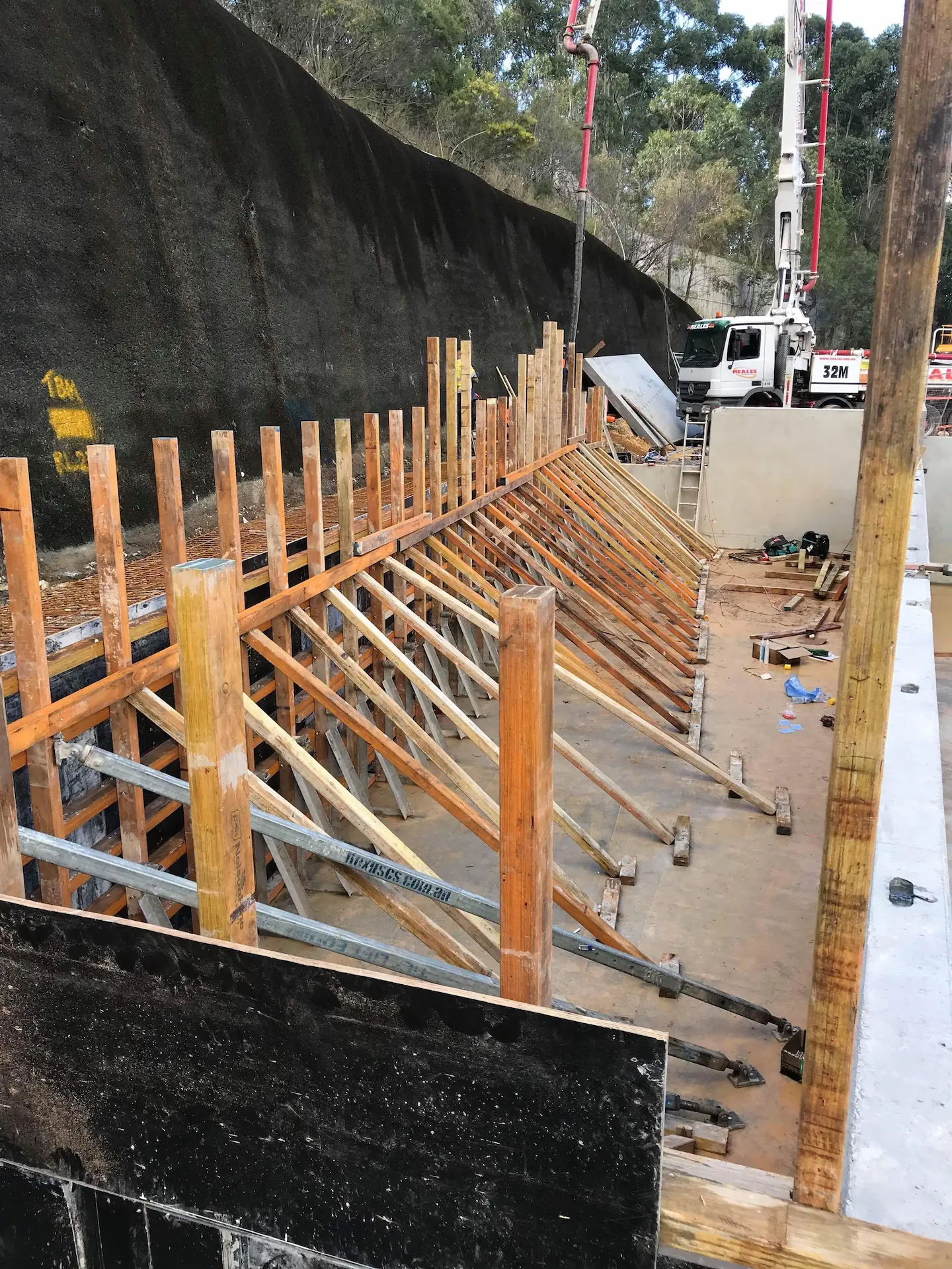 Progression in concreting project displaying wooden formwork for vertical concrete structures in preparation, with construction equipment in the background.