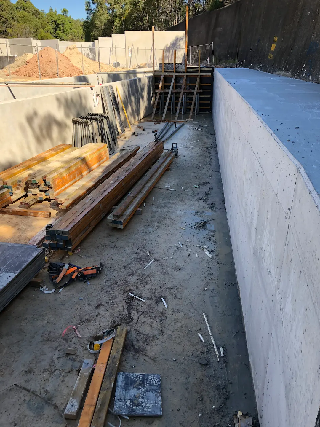 Initial stage of commercial concreting with a clear view of the excavation and concrete formwork set up against a retaining wall on a bright day.