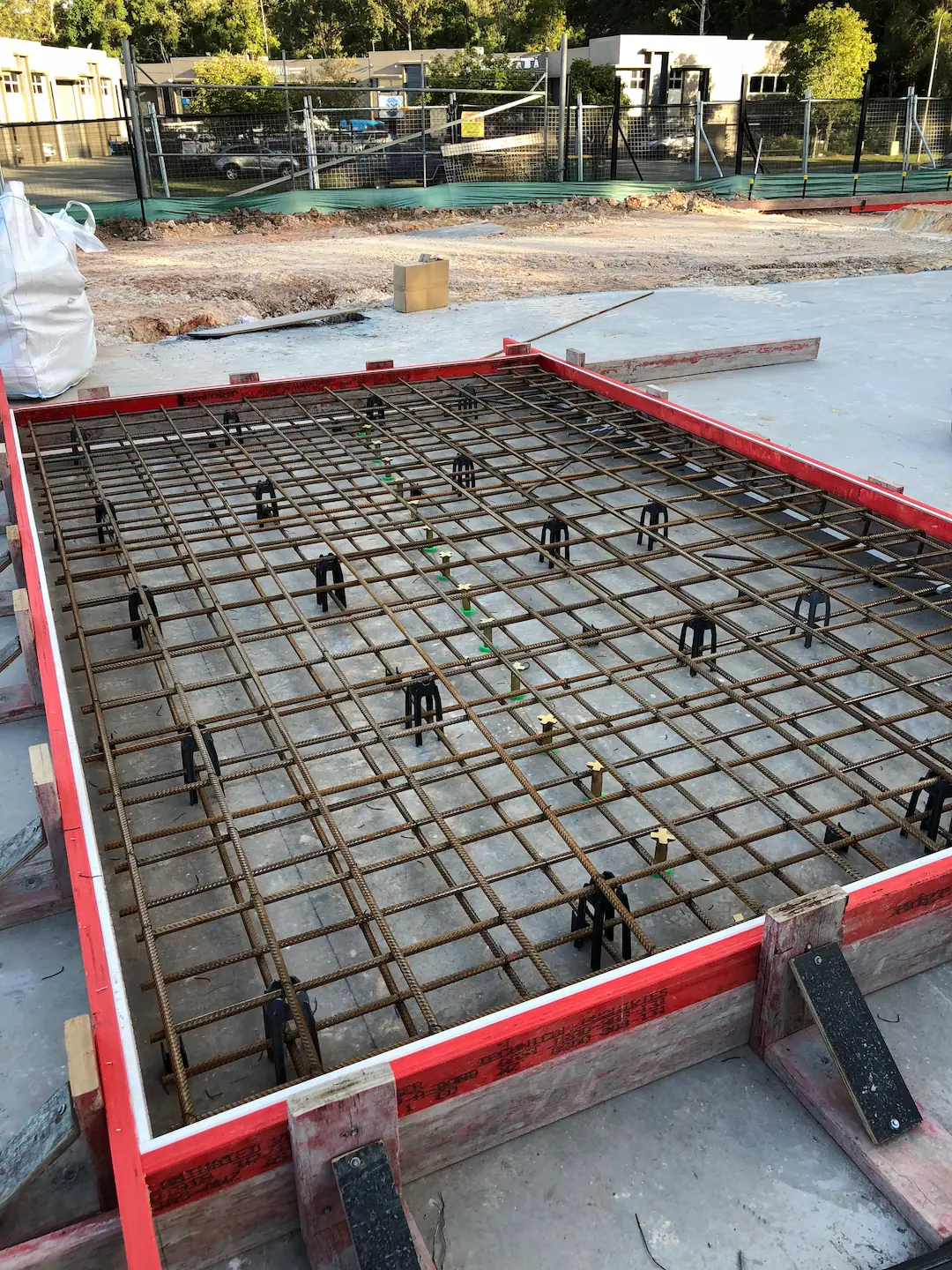 Nearly complete concreting framework showcasing a wide span of reinforcement bars within a wooden formwork perimeter, under clear skies.