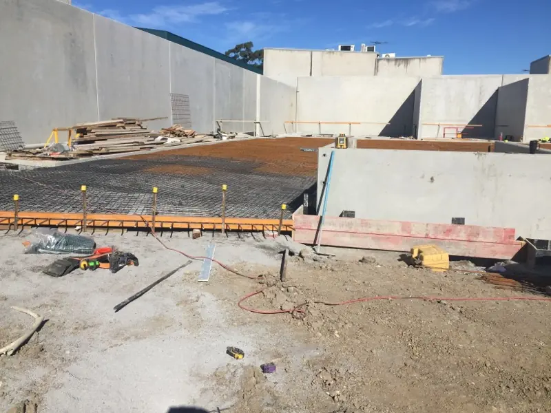 Concrete reinforcement mesh ready on the ground, with construction tools scattered nearby, at the Kirawee project site with precast panels in the background.