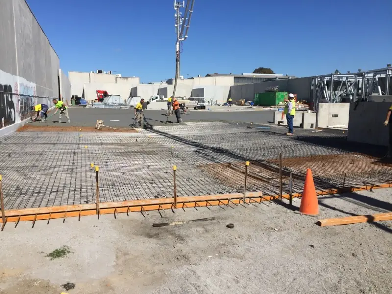 Construction workers evenly spread across the Kirawee job site, working on the reinforcement framework for a large concrete pour under clear skies.