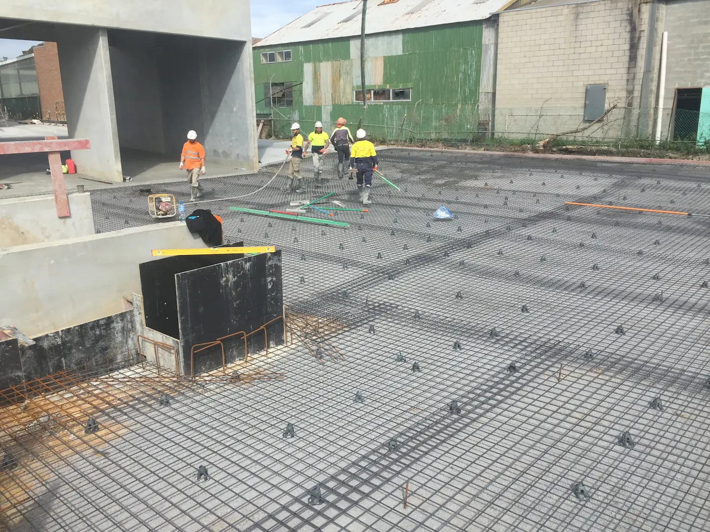 A construction team busily prepares a steel-reinforced area for concrete pouring, surrounded by tall precast concrete walls at Kirawee.