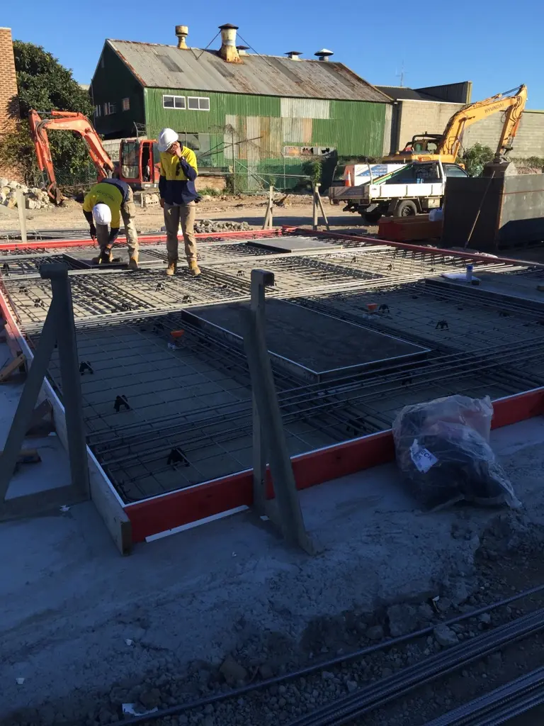 Construction personnel working on reinforcing mesh for a foundation, with concrete formwork in place at the Kirawee project site.