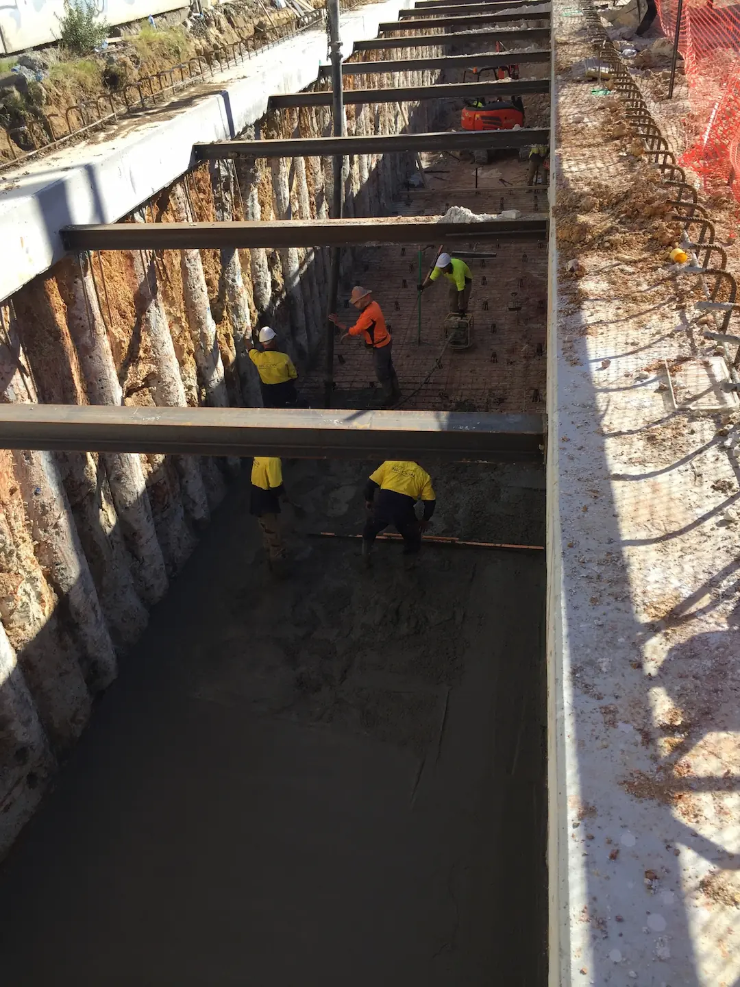 Workers pouring and smoothing concrete into deep trench foundations reinforced with steel at the Kirawee site.