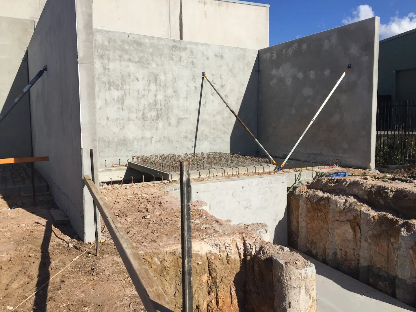 A newly installed concrete panel supported by braces amidst excavation work at the Kirawee construction project.