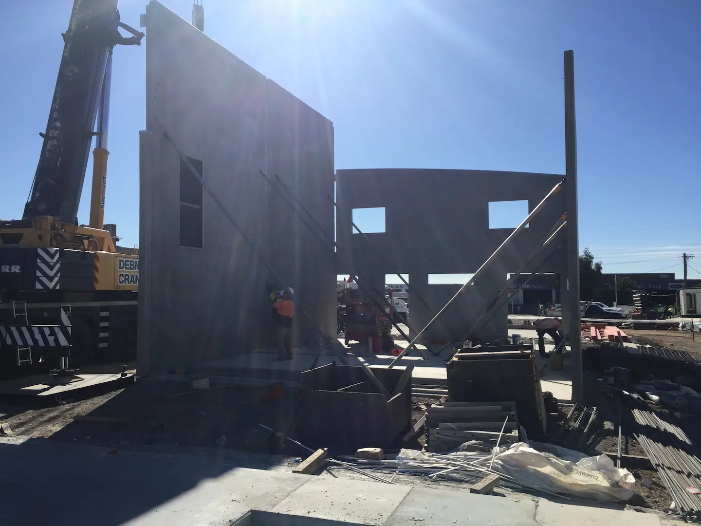 A large concrete panel being hoisted by a crane against a clear sky at the Kirawee commercial construction site.