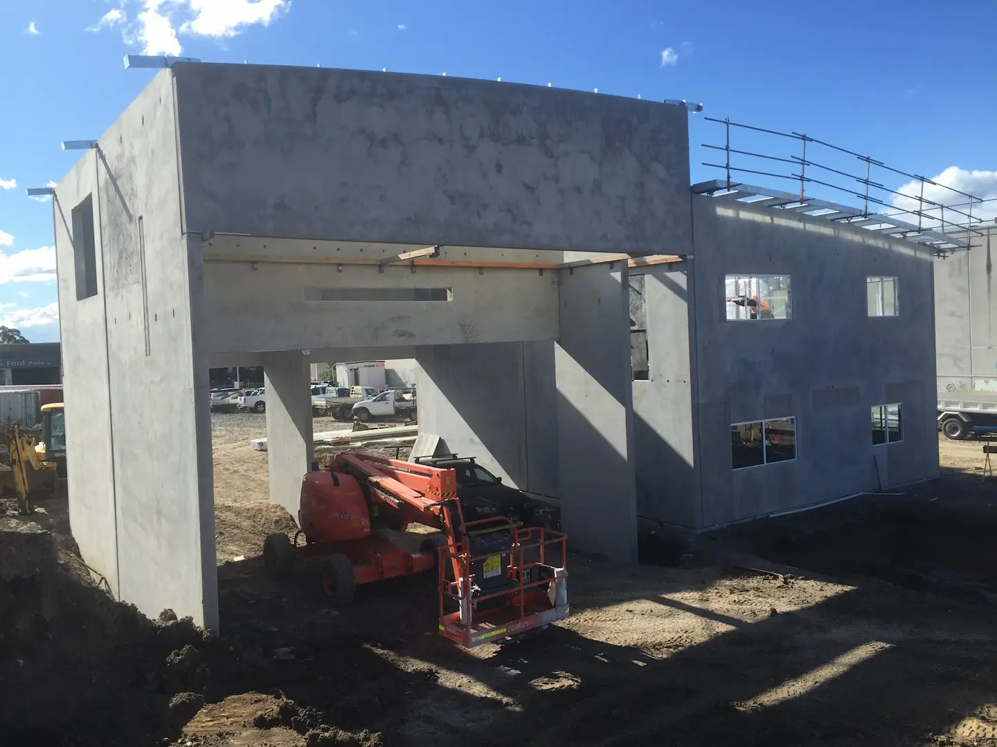 A concrete building structure with panel walls erected and scaffolding in place at the Kirawee project site under a blue sky.