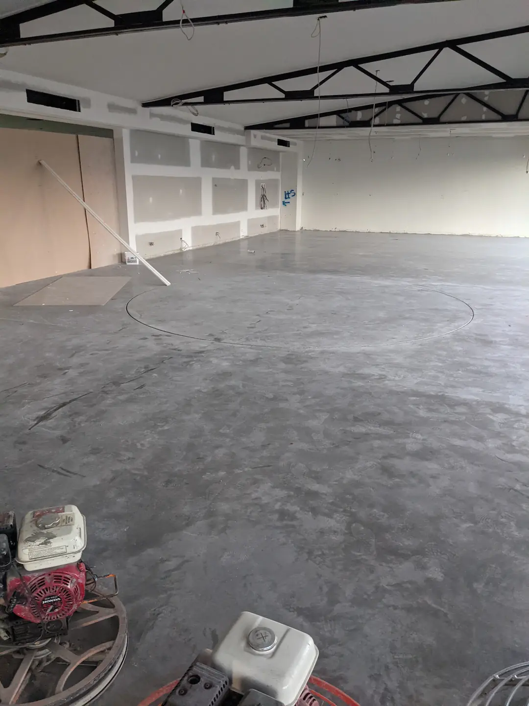 The interior of a commercial Brisbane storage facility under construction with a tall concrete tilt panel being supported by a mobile crane. The shadow of the structure is cast across the concrete floor, segmented by rays of sunlight entering from the open bay doors.